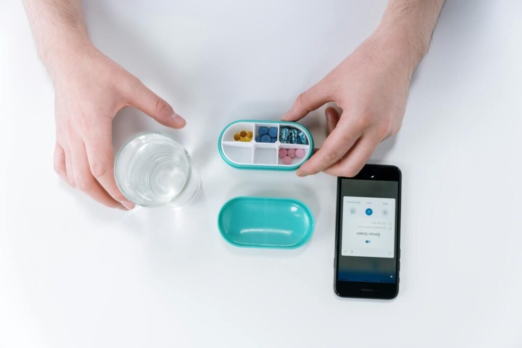 Overhead view of hands using a smartphone app and pill organizer for medication management.